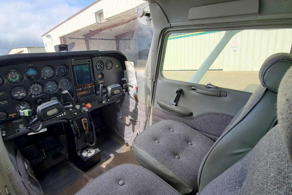 Inside of an empty two seater cockpit with hangar in background.
