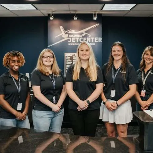 Five women standing and smiling in Columbia Jet Center office.